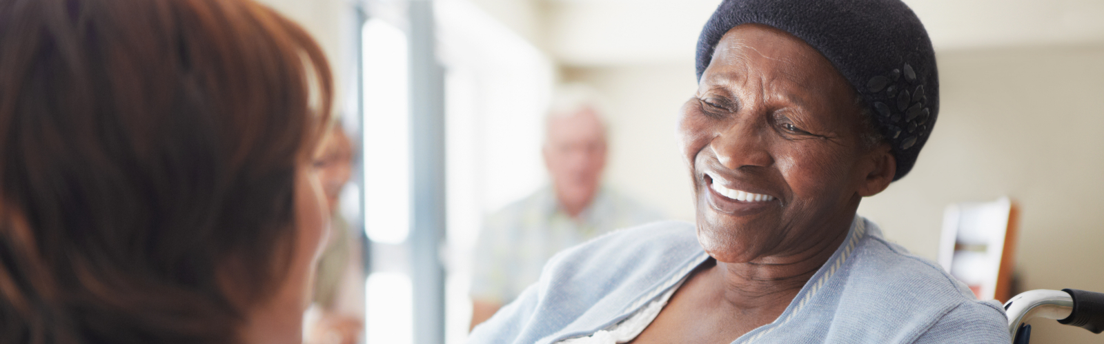 An older Black lady in a wheelchair smiles at her carer