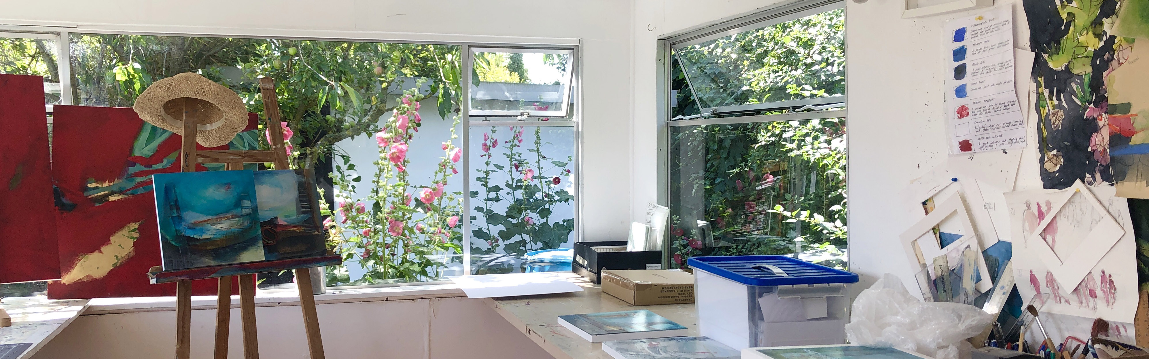 An image of an easel next to a window opening out onto a garden full of pink flowers