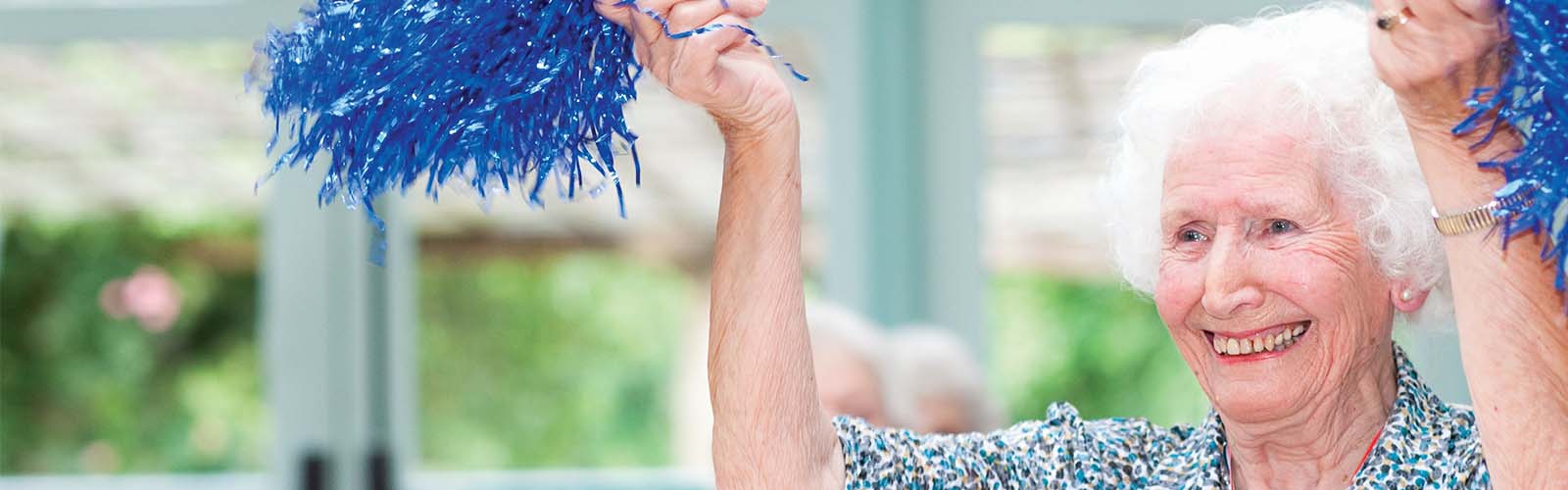 An older lady waves cheerleading pompoms at an Age UK activity class