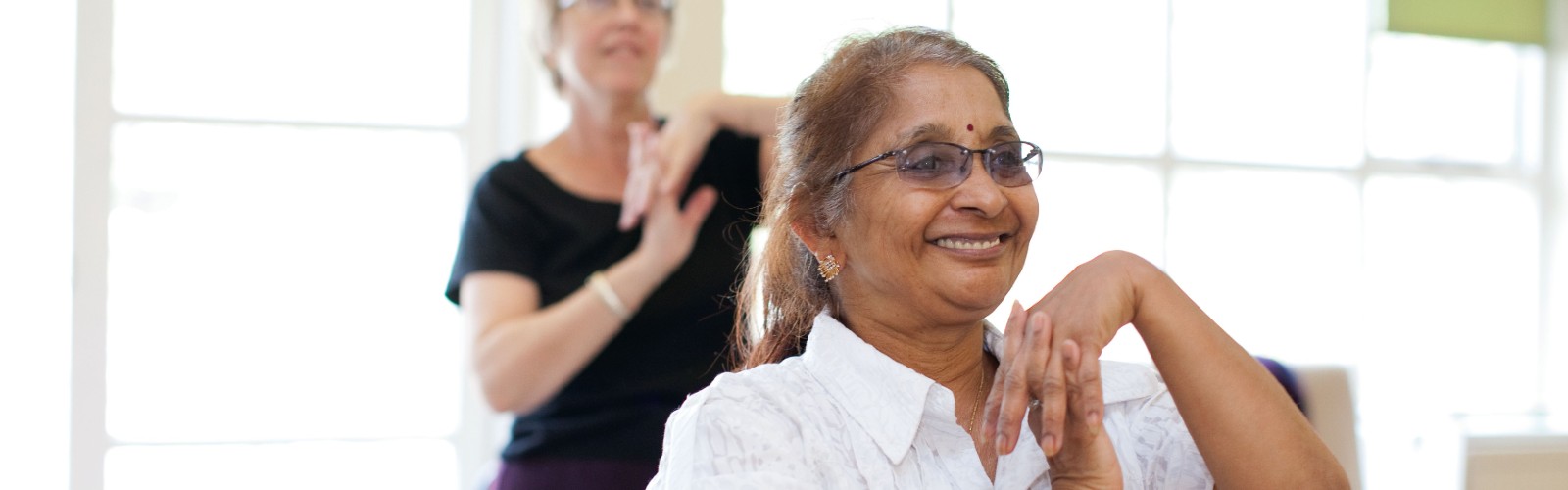 An older Asian lady smiling as she takes part in an Age UK exercise class