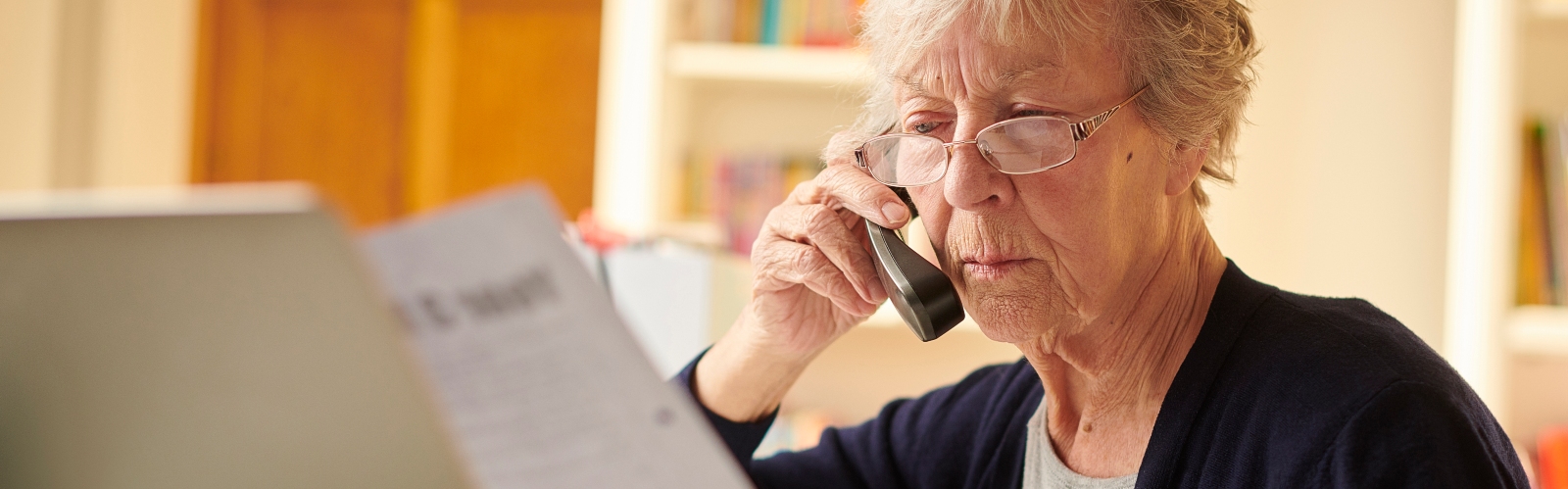An older lady on the phone, looking concerned at her bill