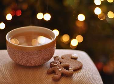 Hot tea and gingerbread biscuit with fairy lights in the background