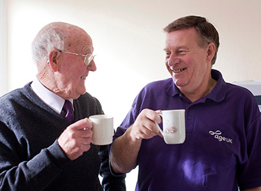 An older man and an Age UK staff member share a cup of tea