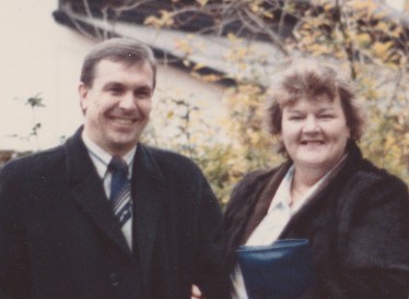 An image of Jamie's grandparents stood in a garden, with their arms linked