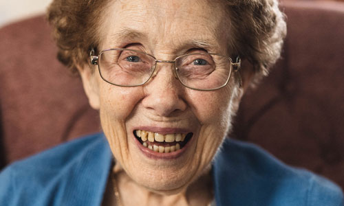 An older lady with reddish hair and glasses grins at the camera