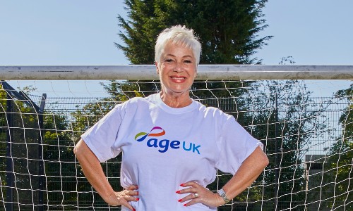Actor Denise Welch wears an Age UK t-shirt, smiling in front of a football net