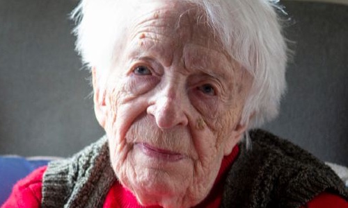 An older woman in a red jumper, looking towards the camera.