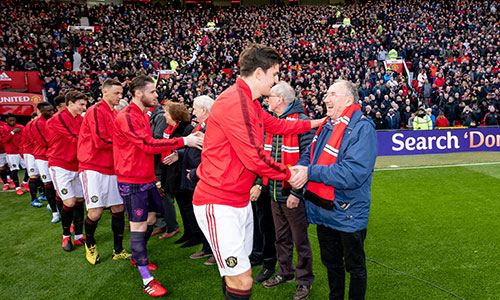 Manchester United players shake holds with older people on the pitch at Old Trafford