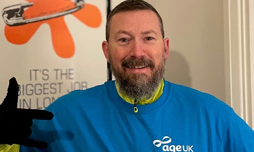 A man with a beard and an Age UK t-shirt looking at the camera 
