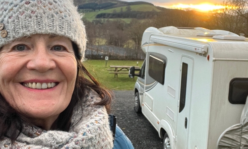 A woman with dark hair grins at the camera, next to her motorhome