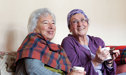 Two women drinking tea while sat on a sofa