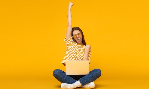 woman sitting in front of a laptop with her hand in the air celebrating a lottery win